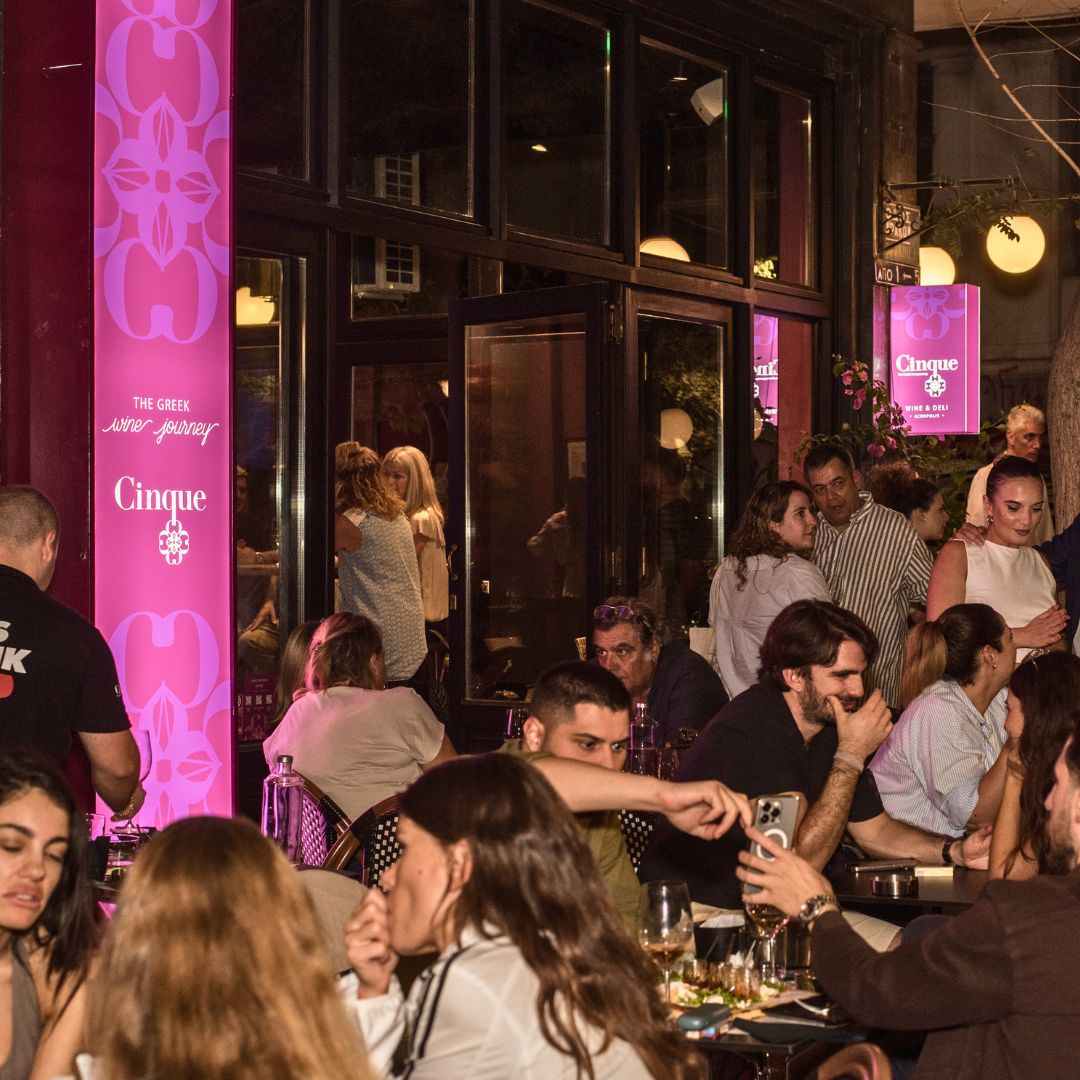 Guests enjoying Greek wine and hospitality at a busy urban Cinque Wine & Deli location in Athens.