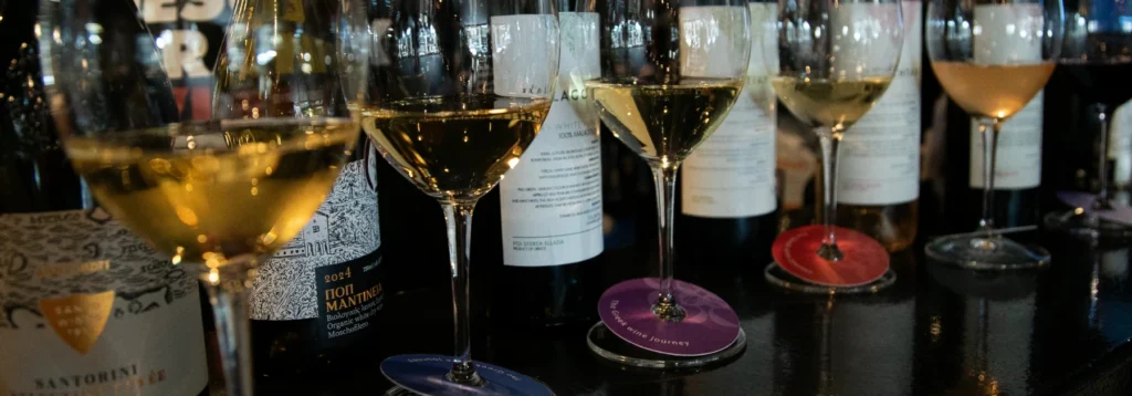 Glasses of white wine and wine bottles on The Greek Wine Journey tasting mats at Cinque.